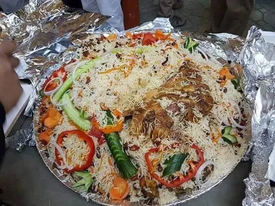 A large platter of biryani garnished with chicken, colorful vegetables, and aromatic rice, served on a silver tray.