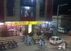 Al-Dubai restaurant exterior at night, featuring bright signage and customers outside with parked motorcycles.
