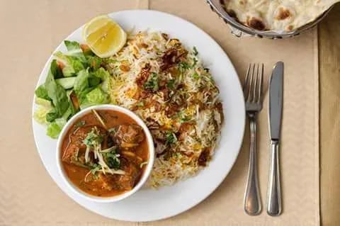 Biryani served with a side of curry, salad, and a lemon wedge, accompanied by naan bread.