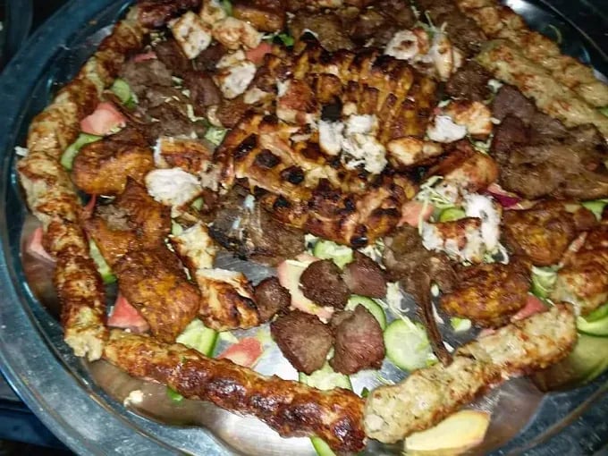 Assorted platter of grilled kebabs, including seekh kebabs and chicken tikka, served on a bed of fresh vegetables.