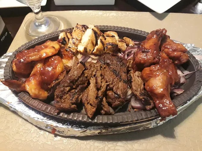 Sizzling platter featuring grilled chicken, beef, and shrimp served with onions.