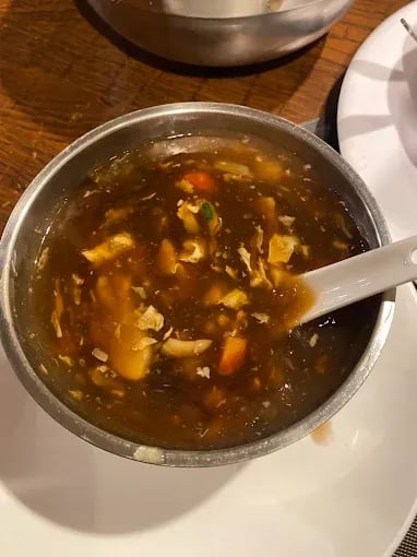 Hot and sour soup served in a metal bowl, featuring vegetables and shredded chicken in a thick, savory broth.