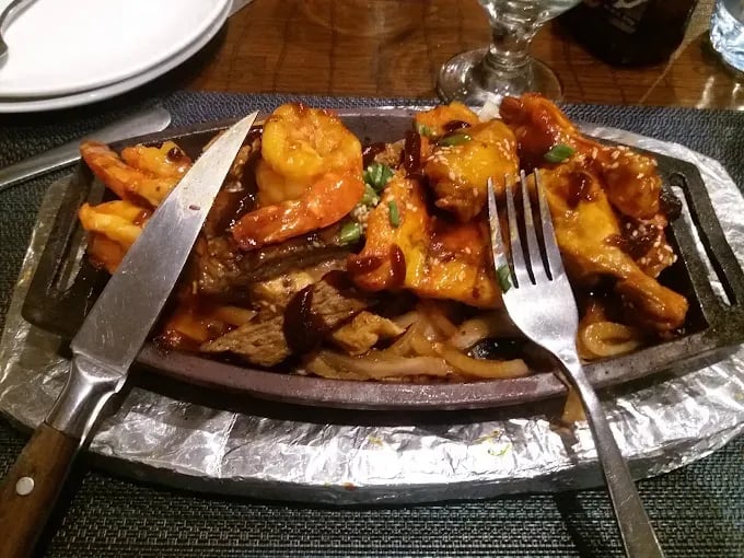 Sizzling platter with grilled shrimp, chicken, and beef served with onions and sauces.