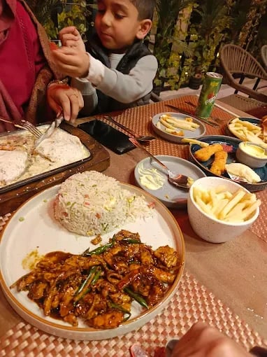 Delicious chicken dish with rice, accompanied by fries and a child reaching for food at a dining table.