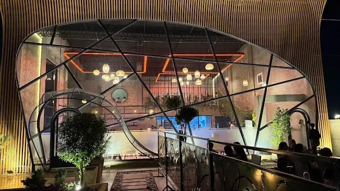 Modern restaurant exterior featuring a unique glass design, illuminated with warm lighting and surrounded by greenery.