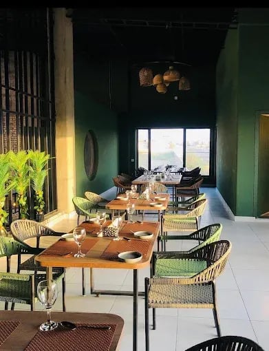 Modern restaurant interior featuring green walls, wooden tables, and stylish chairs, illuminated by natural light.